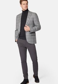 Szary blazer w kratę noszony na czarnym golfie, zestawiony z ciemnymi spodniami i czarnymi botkami za kostkę. Blazer ma szpiczaste klapy i dopasowany krój.