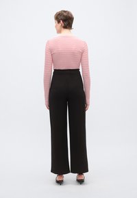 Κόκκινο και λευκό ριγέ μπλουζάκι με μακριά μανίκια συνδυασμένο με μαύρο, ψηλόμεσο παντελόνι με φαρδιά πατζάκια. Λείο υλικό, μίνιμαλ σχεδιασμός και χωρίς εμφανή μοτίβα.