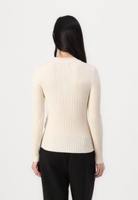 Cream ribbed knit long-sleeve top with a fitted silhouette, round neckline, and a subtle texture, paired with black trousers.