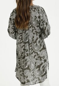 Tunique longue et ample de couleur vert foncé avec un motif cachemire blanc. Elle présente des fentes latérales et un tissu doux et texturé.