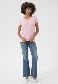 Camiseta rosa de manga corta hecha de una tela suave, combinada con unos vaqueros acampanados de color azul claro. La modelo lleva unos tacones color crema. Look simple y casual.