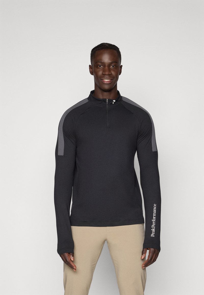 Svart langermet zip-up skjorte med grå skulderdetaljer. Har en tettsittende design og en logo på venstre arm. Glatt tekstur.