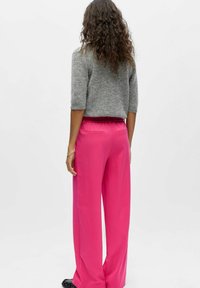 Pull à manches courtes gris associé à un pantalon rose à jambes larges. Le pantalon est doté d'une ceinture élastique et de deux poches arrière.
