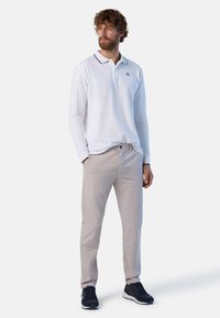 Polo bianco a maniche lunghe con colletto e dettagli blu navy, abbinato a chinos beige e sneakers nere. Design semplice, vestibilità regolare.