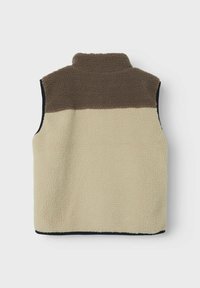 Fleeces vestes ar augstu apkakli, bēšas krāsas ķermeni, brūnu plecu daļu un melniem malām. Mīksta tekstūra, bez redzamām aizdarem.