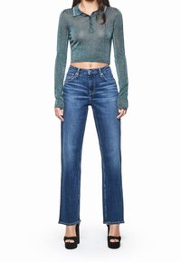 Top de manga larga color verde azulado brillante con cuello, combinado con jeans azules de tiro alto, con pierna recta y dobladillo sin rematar, llevado con tacones de plataforma negros.