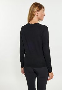 Zwarte gebreide trui met lange mouwen, ribbelzoom en ronde halslijn. Zachte textuur met subtiele stikdetails, gedragen met zwarte strakke broek.