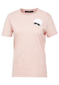 Světle růžové bavlněné tričko s kulatým výstřihem, krátkými rukávy a grafickým designem, který zobrazuje osobu v slunečních brýlích na levé straně hrudi.