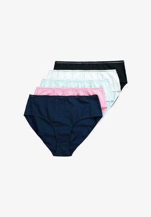 Pewna siebie ciemnoskóra kobieta dopasowuje biały, podtrzymujący biustonosz i pasujące wysokie majtki na jednolitym jasnym tle.