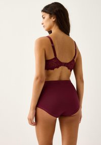 Burgundy spets-bh med justerbara band och matchande högmidjade shorts. Bh:n har en vågig spetskant och slät tyg.