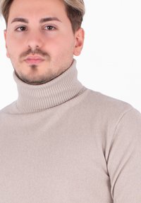 Maglione beige a collo alto a costine con un design aderente, caratterizzato da un colletto alto e un tessuto testurizzato.