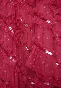 Tissu en tulle rouge avec des couches froncées et des paillettes brillantes, présentant une surface texturée et de petits motifs d'étoiles partout.