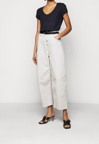 Beige wide-leg pants with a button front, paired with a navy V-neck t-shirt. Black belt and black heeled sandals with a bow detail.