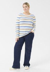 Striped long-sleeve top with blue, beige, and brown lines; ribbed texture. Paired with dark blue jeans and light-colored sneakers.
