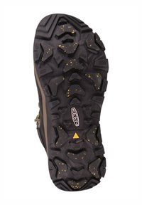 Schwarze Gummisohle mit tiefen Profilrillen, akzentuiert durch gelbe Sprenkel. Verfügt über ein ausgeprägtes Zickzackmuster für Halt und Stabilität.