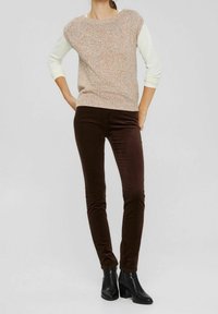 Pull en tricot à motif moucheté multicolore, col rond et manches courtes, associé à un pantalon en velours côtelé marron ajusté et des bottines.