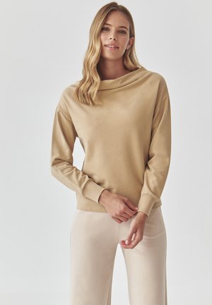 Beige sweatshirt with a cowl neck, long sleeves, and ribbed cuffs. Smooth texture, casual style, paired with beige pants.