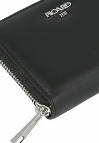Portefeuille en cuir noir avec quincaillerie en argent, doté d'une fermeture éclair et d'une finition texturée. Logo embossé sur le devant.
