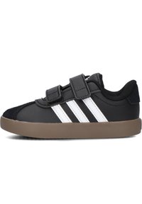 Černé tenisky s bílým designem tří pruhů, se semišovou špičkou a nastavitelnými suchými zipy, umístěné na hnědé gumové podrážce.