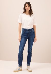 Blauwe denim jeans met een slim fit en een middenhoge taille, gecombineerd met een witte t-shirt en witte sneakers met blauwe accenten.