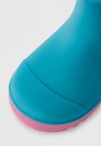 Botte de pluie en caoutchouc bleu avec un bout arrondi, semelle en caoutchouc rose texturée et un corps lisse. Présente un design sans coutures et un contraste de couleurs marqué.