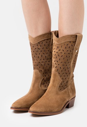 Bruine suède cowboylaarzen met complexe bloemmotieven, een spitse neus en een gestapelde hak. Voorzien van gestikte accenten langs de bovenkant.