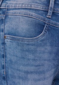 Jeans de mezclilla azul deslavada con un bolsillo trasero con remache plateado y costuras en contraste a lo largo de las costuras. Tela suave y texturizada.