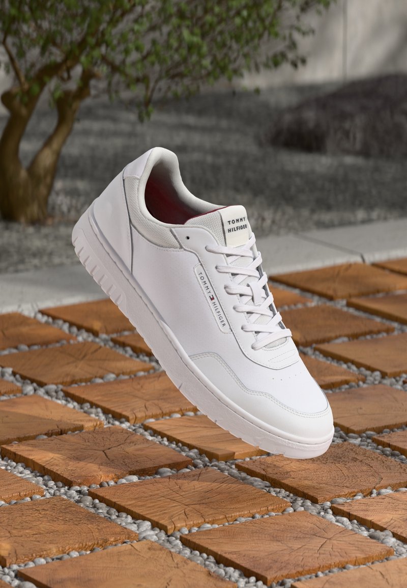 Baskets en cuir blanc à texture lisse, à lacets, avec une étiquette de marque sur le talon et une semelle en caoutchouc blanche unie.