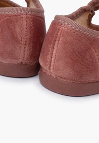 Zapatillas de terciopelo rosa suave con una textura lisa, forma redonda y una suela blanda reforzada. Los bordes están acabados con un ribete de tela a juego.