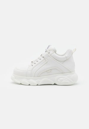 Biały masywny sneaker z grubą podeszwą, sznurowanym przodem, wyściełanym kołnierzem i pętelką z tyłu, widoczny z zewnętrznej strony.