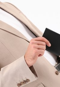 Beige Leinenanzugjacke mit drei braunen Knöpfen am Ärmel, Hand, die eine schwarze Brieftasche hält, vor einem weißen Hintergrund.