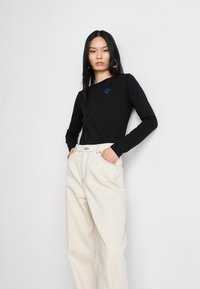 Black long-sleeve top featuring a blue circular logo, paired with high-waisted off-white wide-leg pants with contrast stitching.