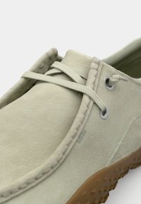 Zapato de cuero verde claro con una superficie suave y texturizada, con ojales de metal, costuras en contraste y una suela de goma marrón texturizada para mayor agarre.