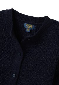 Cardigan lavorato a maglia blu navy con finitura testurizzata, dotato di scollatura a V, chiusura con bottoni e un'etichetta che indica la taglia per bambini.