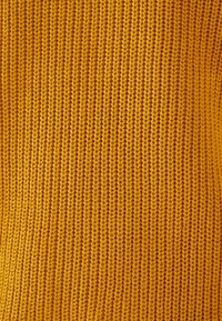 Strickstoff in einem satten Senfgelb zeigt eine feine Rippenstruktur mit gleichmäßig verteilten vertikalen Linien, die ein weiches, warmes Erscheinungsbild erzeugt.