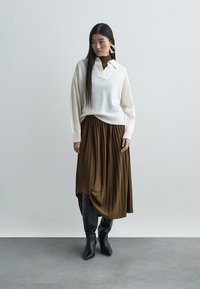 Λευκό πλεκτό πουλόβερ με γιακά, συνδυασμένο με καφέ πλισέ φούστα και μαύρες μπότες μέχρι το γόνατο. Το σύνολο διαθέτει υφασμένο σχέδιο και κομψή σιλουέτα.