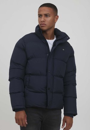 Navy puffer jacket with zip and snap closure, high collar, and quilted design. The fabric appears smooth and insulated, featuring a logo detail.