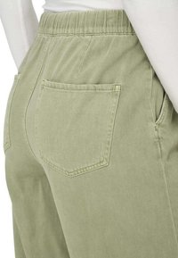 Pantalons en coton vert avec une taille élastique, dotés de deux poches arrière et d'une texture lisse, montrés de côté.