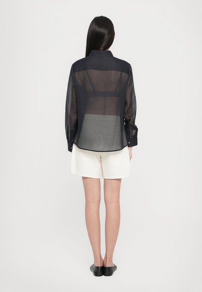 Sheer dark blue button-up shirt with vertical stripes, long sleeves, and a high collar, paired with white shorts.