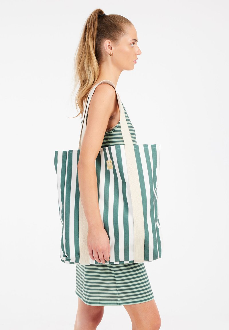 Gestreepte tote bag in groen en wit, gemaakt van duurzaam stof, met dubbele schouderbanden en een rechthoekige vorm.