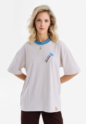Jasnoszara, oversize koszulka z turkusowym okrągłym dekoltem, z niebieskim motywem kwiatowym i czarnym tekstem z przodu. Proste detale przeszyć.