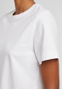 T-shirt blanc en coton à manches courtes avec un col rond. Le tissu a une texture lisse et une coupe décontractée, idéale pour un look casual.