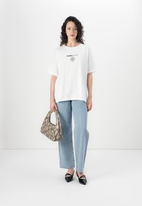 T-shirt oversized branca com texto preto, jeans azul-claro com embellishments prateados, e uma bolsa bege com padrão de cobra. Sapatos pretos de bico fino.
