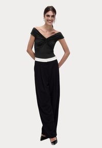 Sort off-the-shoulder bodysuit med tvistet front, parret med højtaljede, løse sorte bukser med hvid talje.