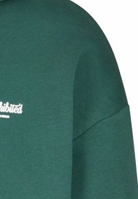 Sudadera verde de manga corta hecha de tela texturizada, con un logo impreso blanco en la parte delantera y un corte relajado.