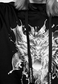 Schwarzer Kapuzenpulli mit einem metallischen Grafikdesign, das Elemente eines Löwen und Wasserspritzern zeigt, ausgestattet mit Kordeln, die mit "JUSTCAVALLI" beschriftet sind.