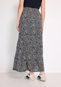 Maxi-Rock in schwarz-weißem Blumenmuster, fließender Stoff mit weit auslaufendem Saum, kombiniert mit beigen und schwarzen Sneakers für einen lässigen Stil.