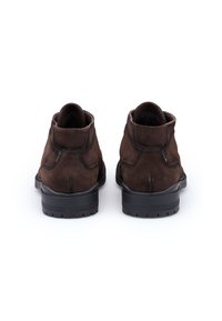 Braune Wildleder-Stiefeletten mit rundem Zehenbereich, kontrastierender schwarzer Gummisohle und dezenten Steppnähten. Glatte Textur mit mattem Finish.