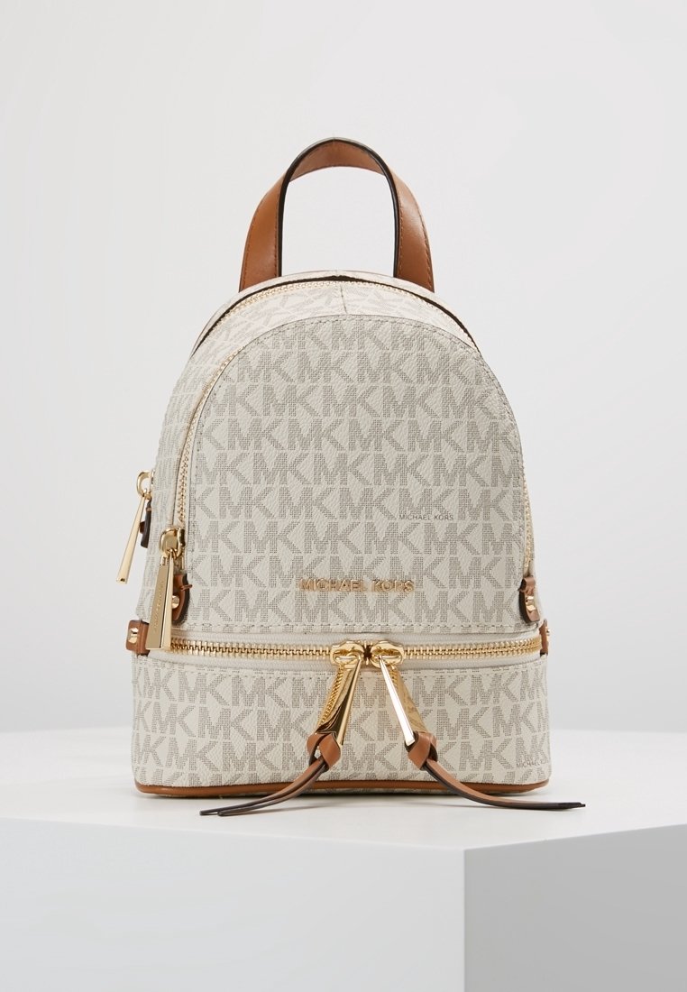 Petit sac à dos beige Michael Kors avec fermetures éclair dorées, poignée en cuir marron et motif répétitif du logo MK.