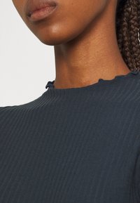Top a coste navy con scollo scallop. Il tessuto ha una texture liscia con linee verticali, che sottolineano il suo design aderente.